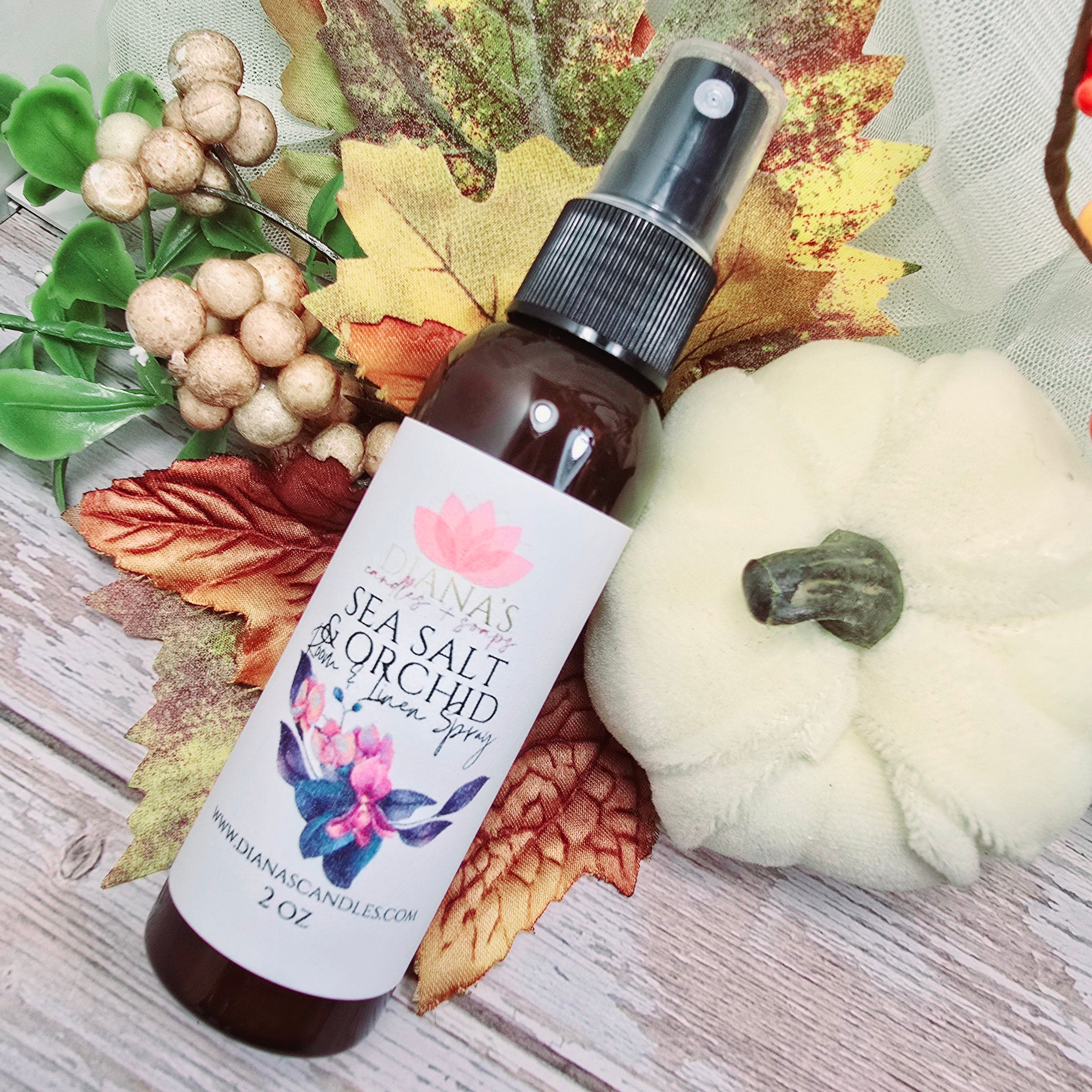 Bottle of 'Sea Salt & Orchid' body spray with a floral label on a wooden surface with autumn leaves and berries.